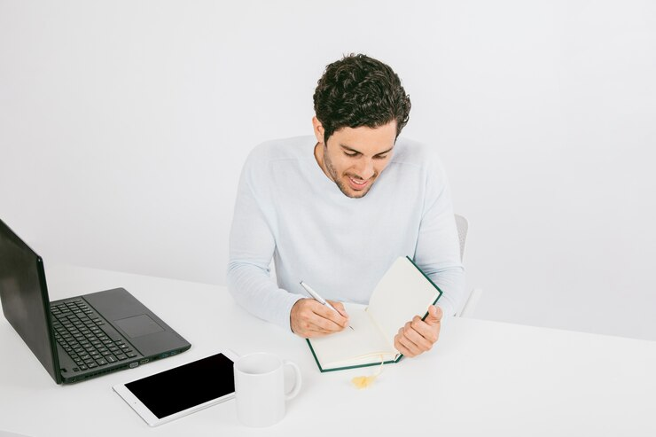 Laptop, tablet and businessman writing on his diary